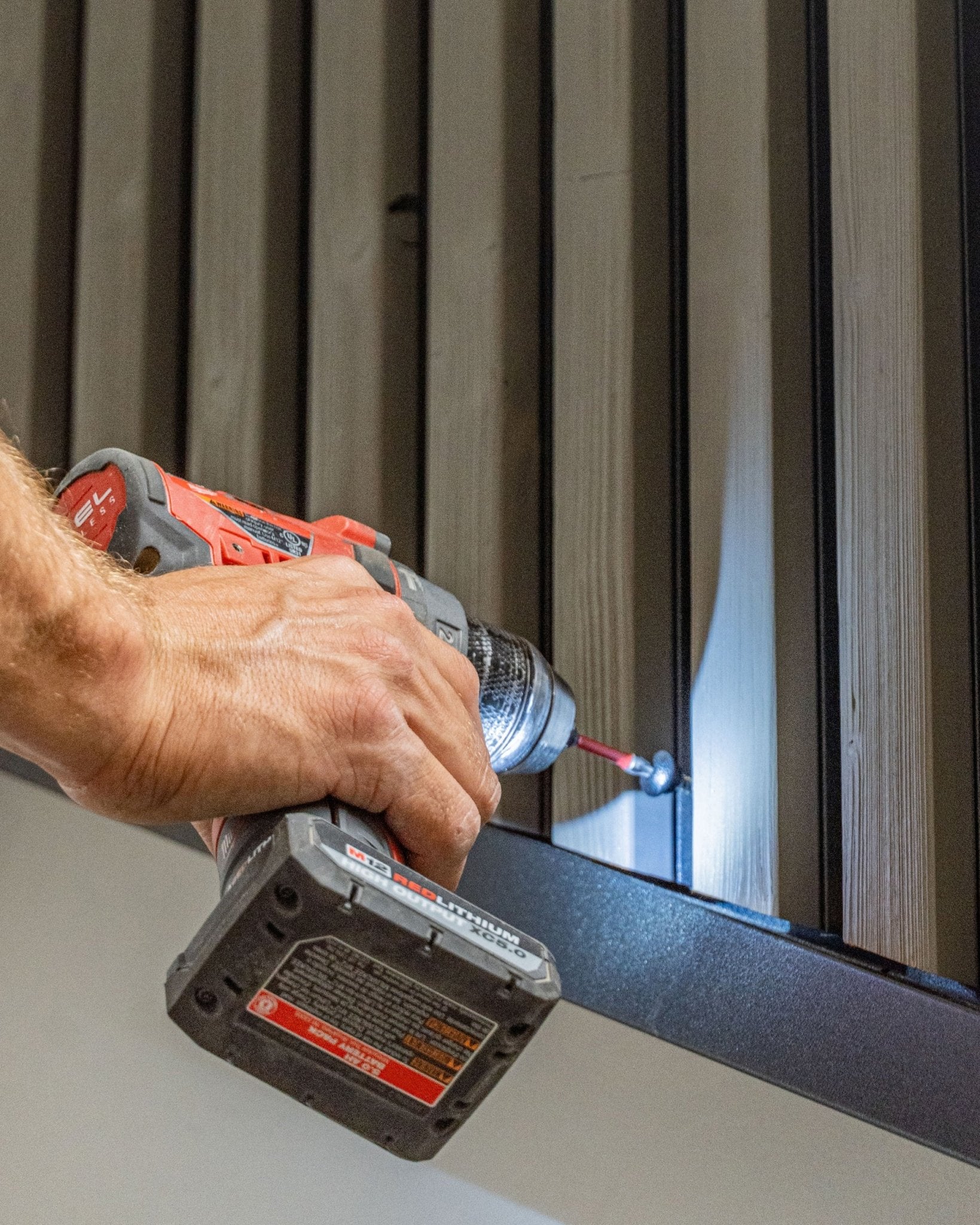 Osoba mocuje black wkręt czołowy WoodUpp (4.8x35, podkładka Ø9.5) do panelu elewacyjnego vertical Aluwood za pomocą wkrętarki akumulatorowej.